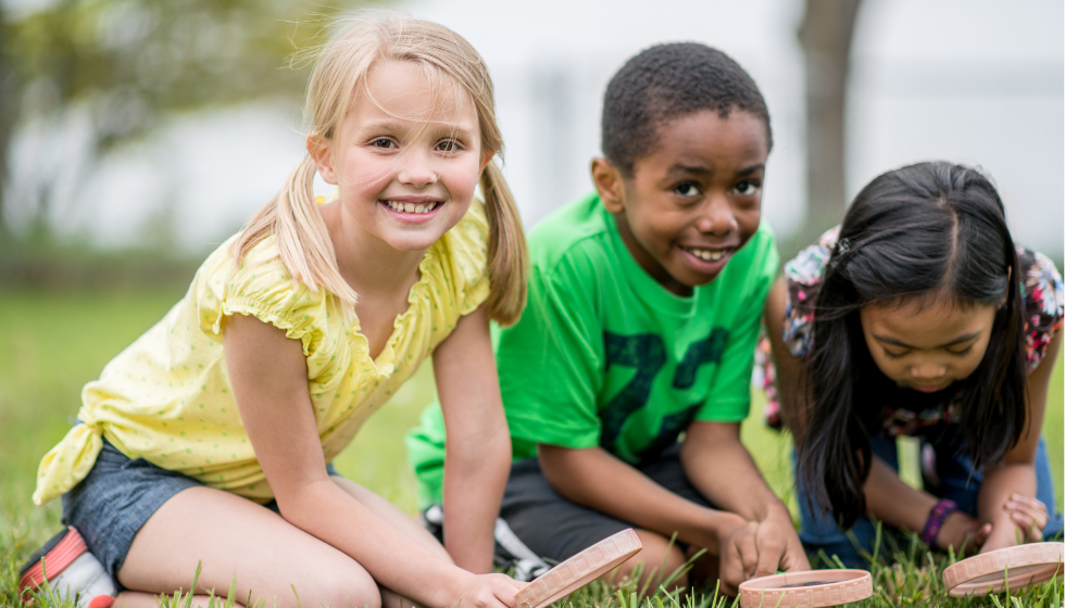 Three kids playing in grass with magnifying glasses