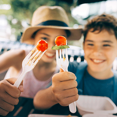 Two smiling kids showing fresh fruits on their forks