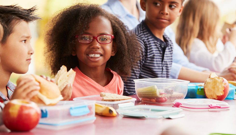 Several smiling students in a row eating lunch