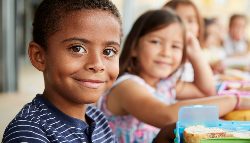 Several smiling students in a row eating lunch
